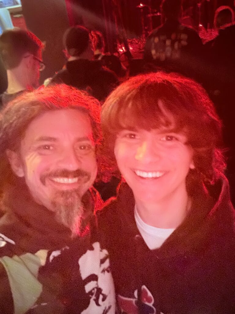 Ben Hoffman and his son smiling together at a concert, bathed in red stage lighting