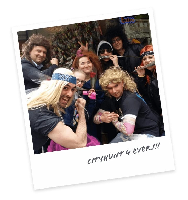Group of cityHUNT participants wearing rock-star wigs and costumes posing together during a team-building scavenger hunt event
