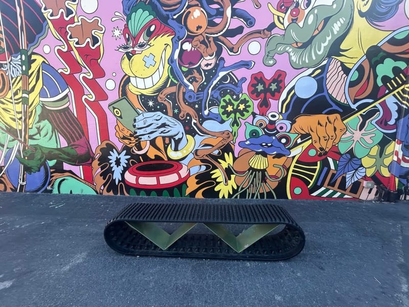 Black metal sculptural bench in front of a bold street art mural featuring colorful cartoon characters